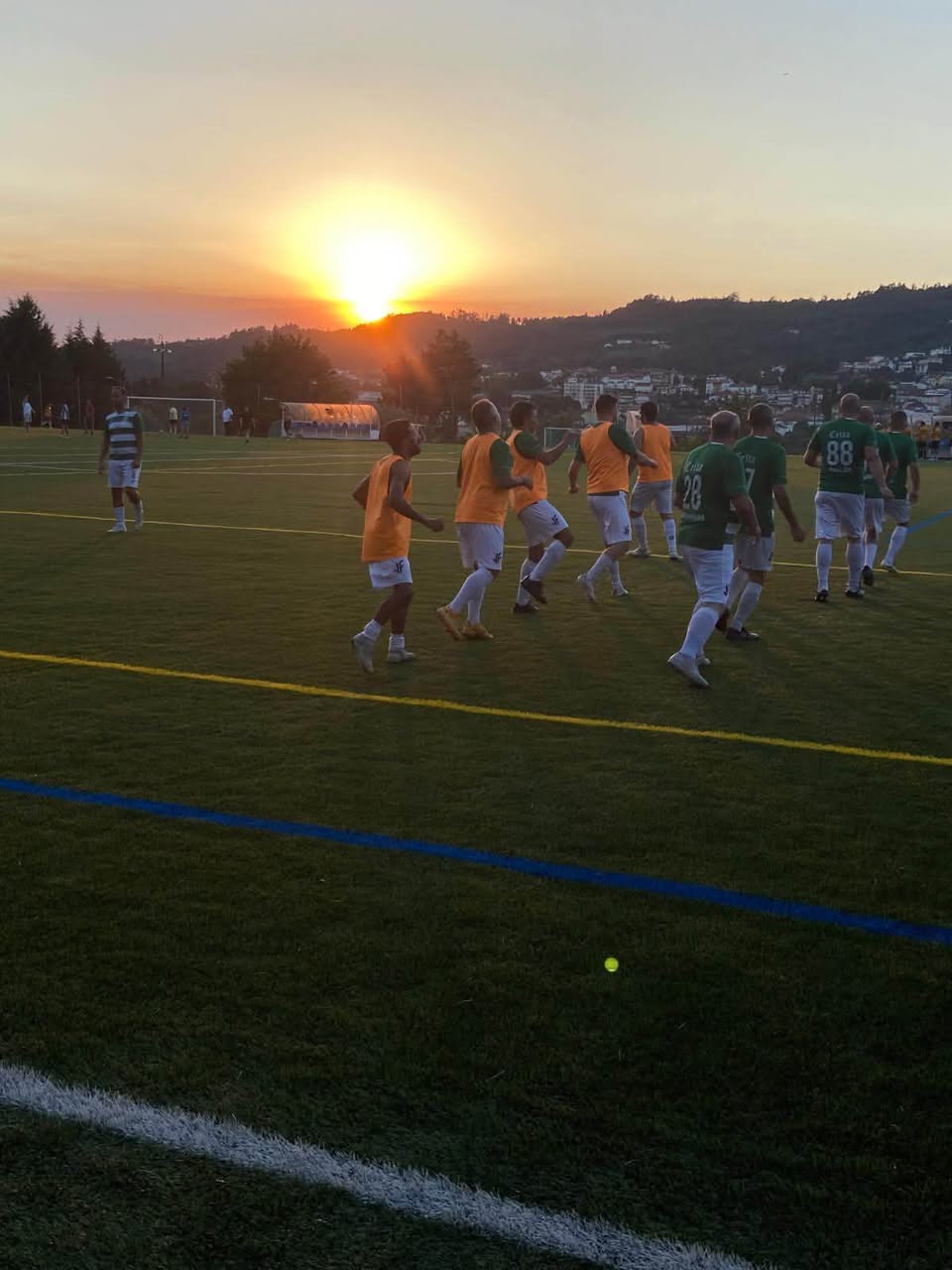 Jogadores dos Leões da Beira em movimento no relvado, ao pôr do sol, no encontro com o Sampedrense.